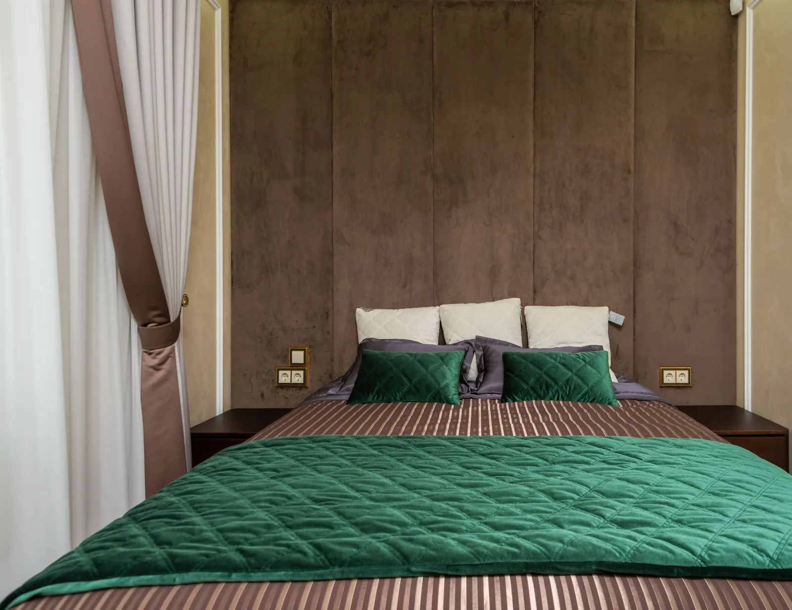Cama con colcha de terciopelo verde esmeralda, cojines crema y cabecero tapizado