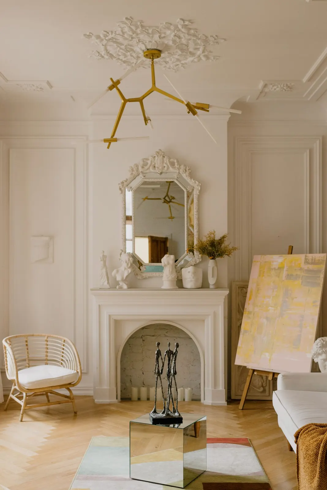 Salón clásico crema con chimenea, molduras, espejo dorado y lámpara de latón